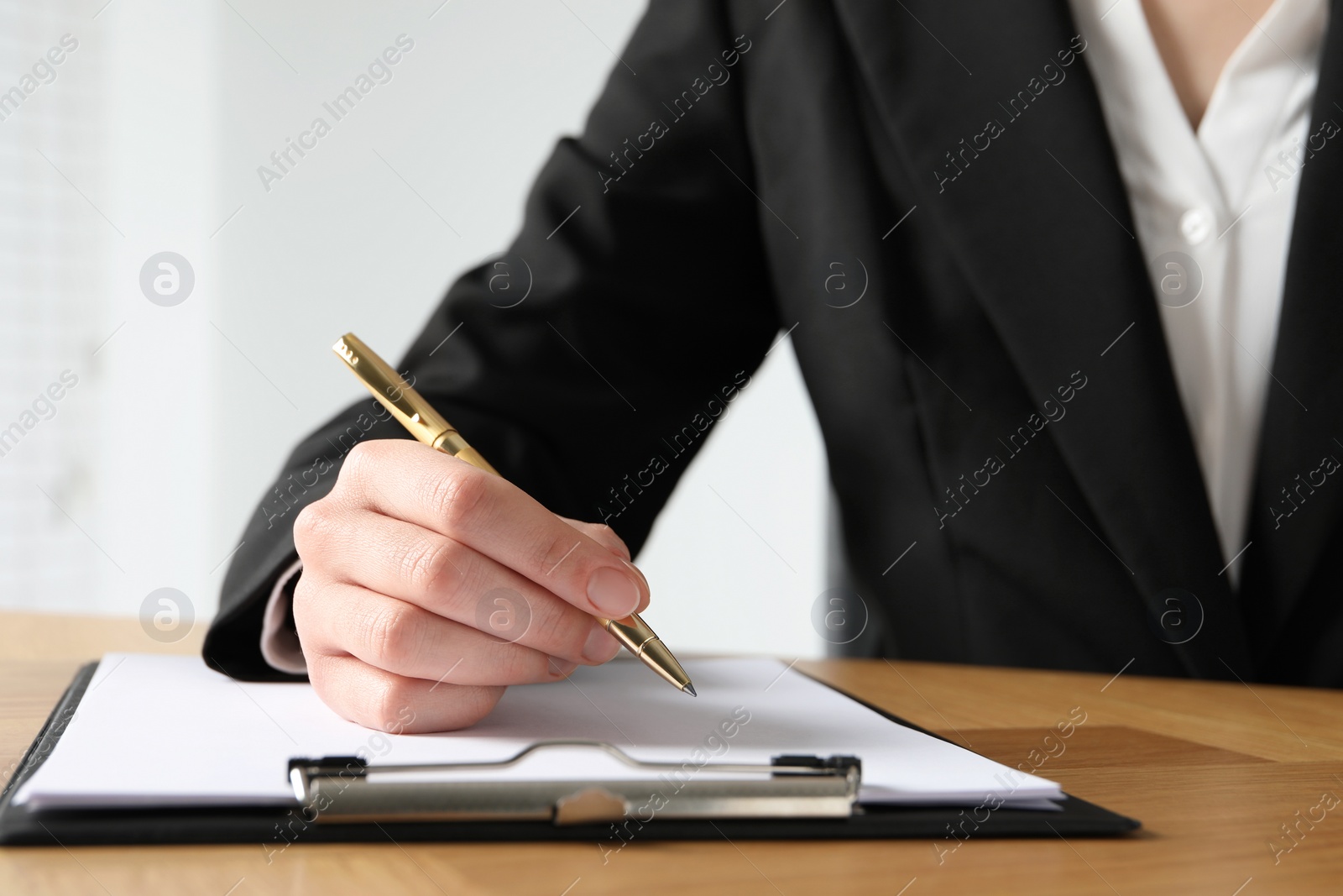 Photo of Woman with pen and clipboard at wooden table, closeup