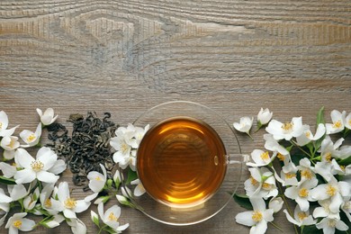 Photo of Glass cup of aromatic jasmine tea, dry leaves and fresh flowers on wooden table, flat lay. Space for text