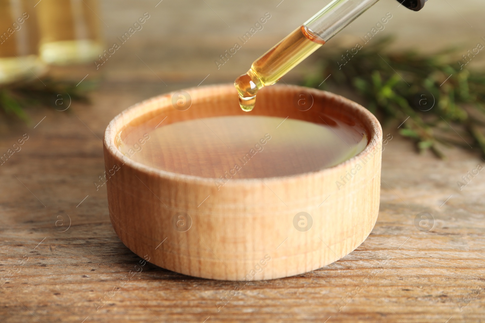 Photo of Dripping natural tea tree oil from bottle into bowl on table, closeup