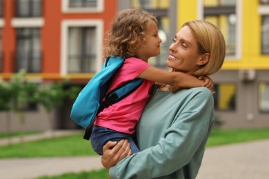 Photo of Happy woman hugging with her daughter near kindergarten outdoors