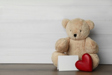 Photo of Cute teddy bear with heart and blank card on wooden table, space for text. Valentine's day celebration