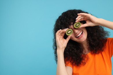 Woman covering eyes with halves of kiwi on light blue background, space for text