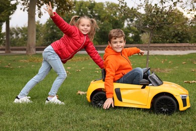 Cute girl pushing children's car with little boy in park