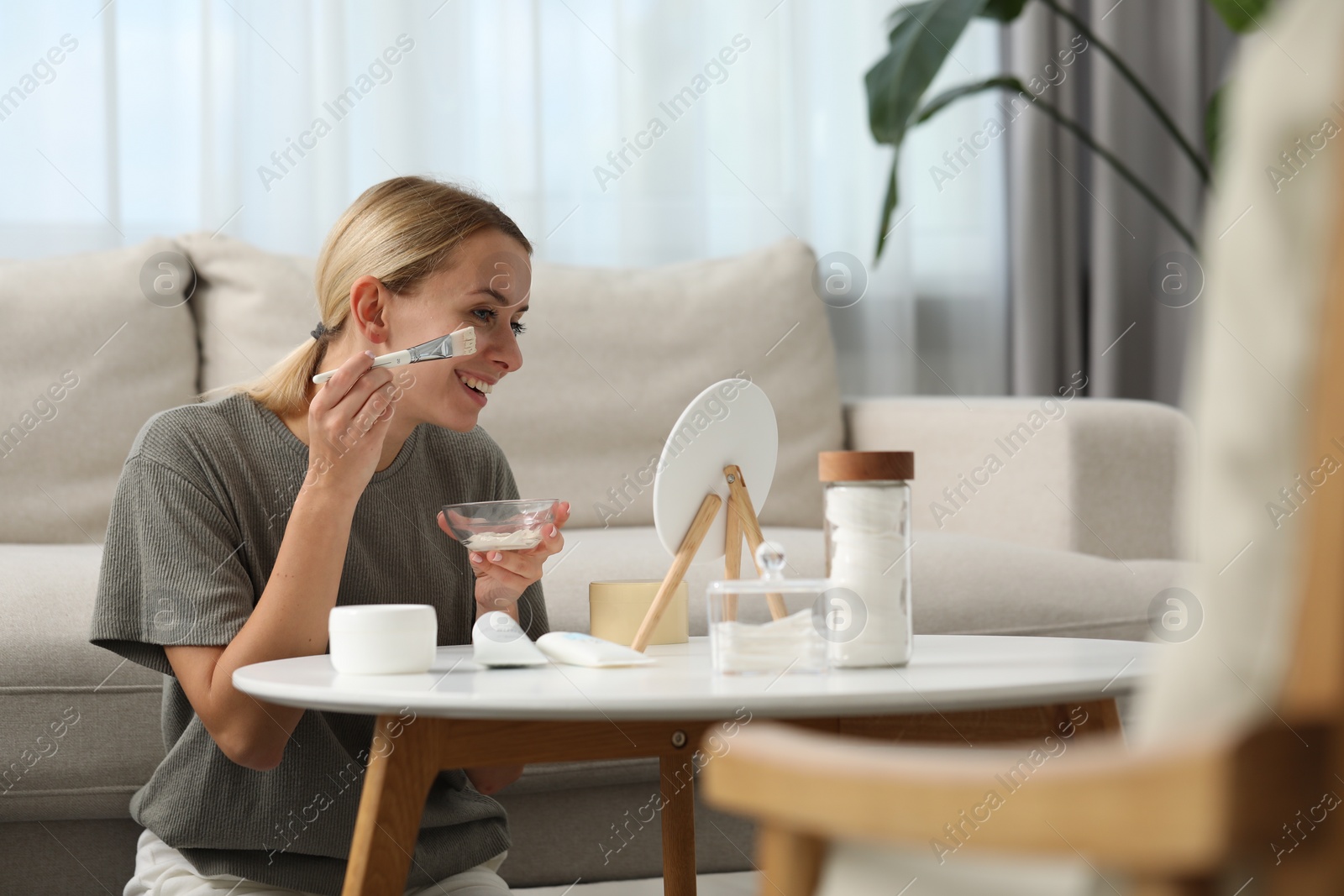 Photo of Young woman applying face mask in front of mirror at home. Spa treatments