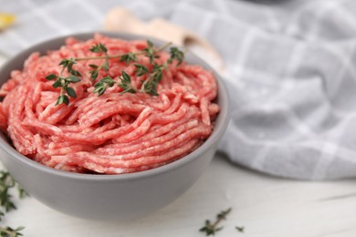 Photo of Fresh raw ground meat and thyme in bowl on white table, closeup. Space for text