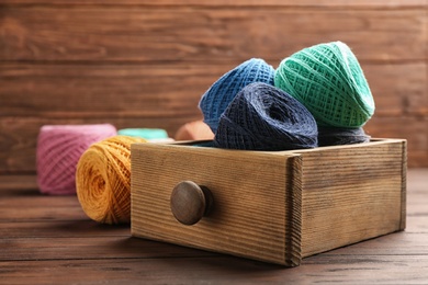 Photo of Colorful clews of threads in drawer on table against wooden background