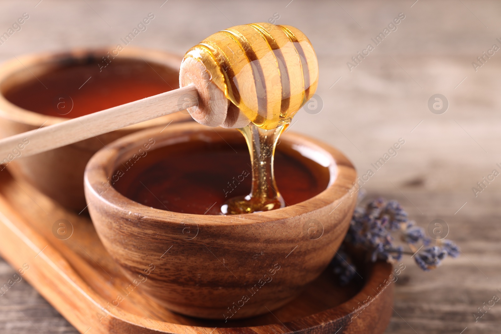Photo of Pouring delicious honey from dipper into bowl on wooden table, closeup