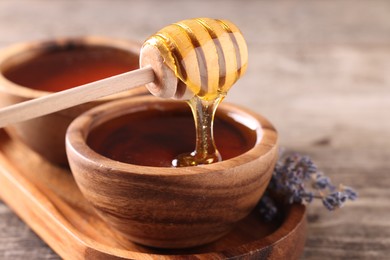 Photo of Pouring delicious honey from dipper into bowl on wooden table, closeup