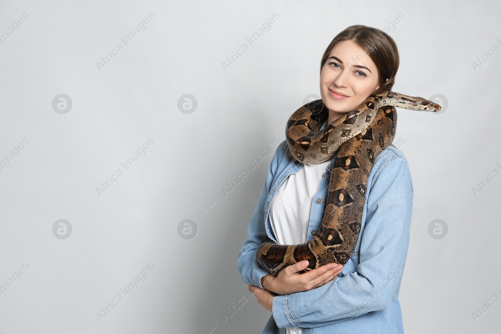 Photo of Young woman with boa constrictor on light background, space for text. Exotic pet