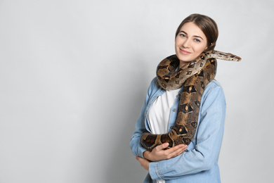 Young woman with boa constrictor on light background, space for text. Exotic pet