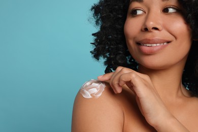 Young woman applying body cream onto shoulder on light blue background. Space for text
