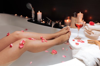 Photo of Woman taking bath with rose petals, closeup. Romantic atmosphere