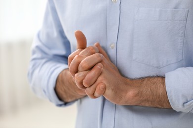 Man cracking his knuckles on blurred background, closeup. Bad habit