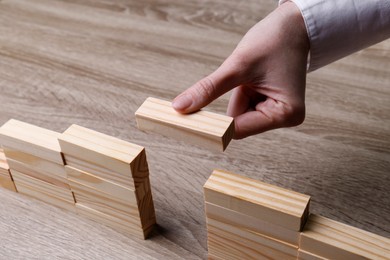 Photo of Woman building bridge with wooden blocks at table, closeup. Connection, relationships and deal concept
