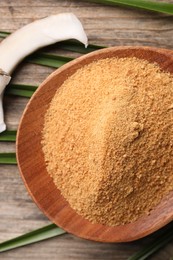 Coconut sugar in bowl, slice of fruit and palm leaves on wooden table, flat lay