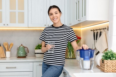 Photo of Woman with glass of water and filter jug in kitchen