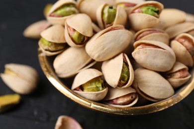 Photo of Tasty pistachios in bowl on black table, closeup