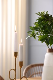 Photo of Burning candles and vase with green branches on blurred background, closeup