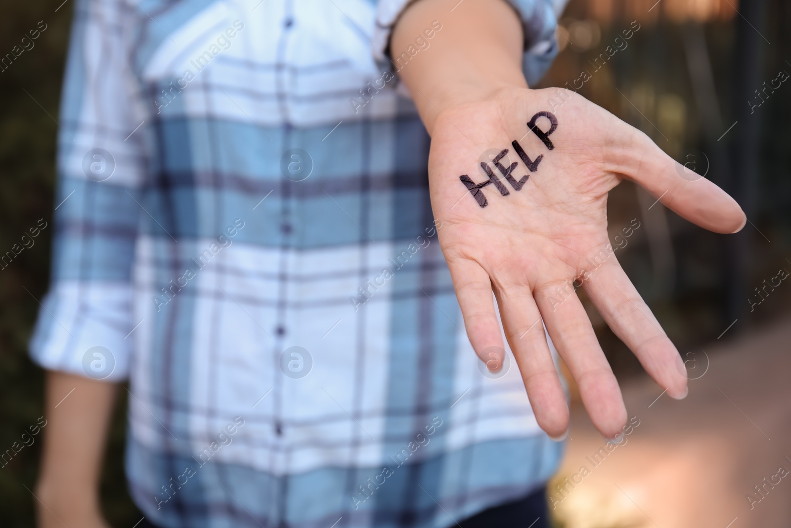 Photo of Woman showing hand with word "HELP" outdoors, closeup