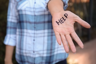 Photo of Woman showing hand with word "HELP" outdoors, closeup