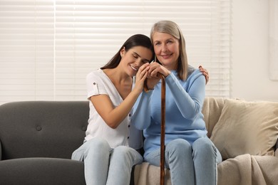 Photo of Mature lady with walking cane and young woman on sofa at home