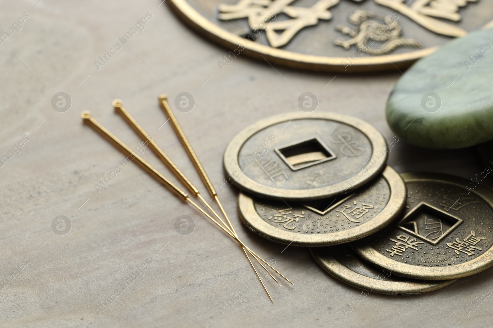 Photo of Acupuncture needles and Chinese coins on beige marble table, closeup