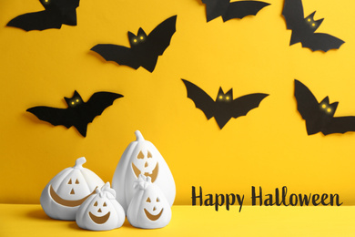 Image of Happy Halloween greeting card design. Jack-o-Lantern candle holders and paper bats on yellow background
