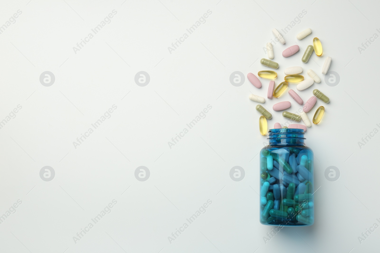 Photo of Vitamin pills and bottle on light background, top view. Space for text