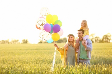 Photo of Happy family with colorful balloons in field on sunny day