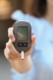 Photo of Woman holding digital glucometer on blurred background. Diabetes control