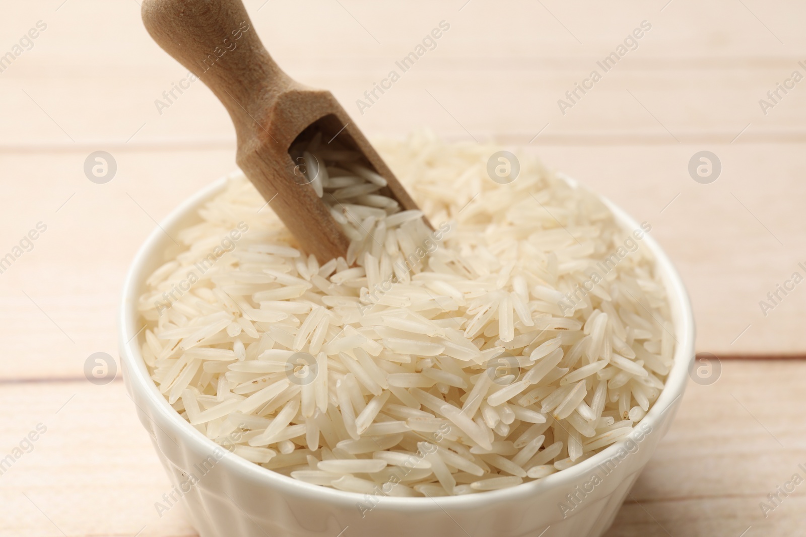 Photo of Raw basmati rice and scoop in bowl on white wooden table, closeup