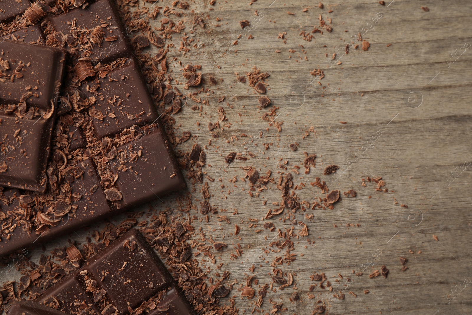 Photo of Pieces and shavings of tasty chocolate bars on wooden table, flat lay. Space for text