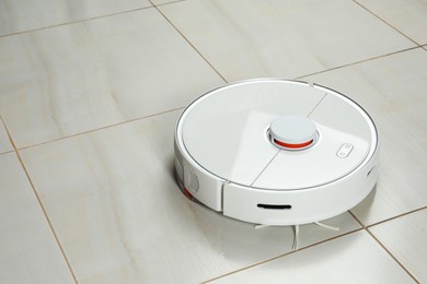 Robotic vacuum cleaner on white tiled floor, space for text