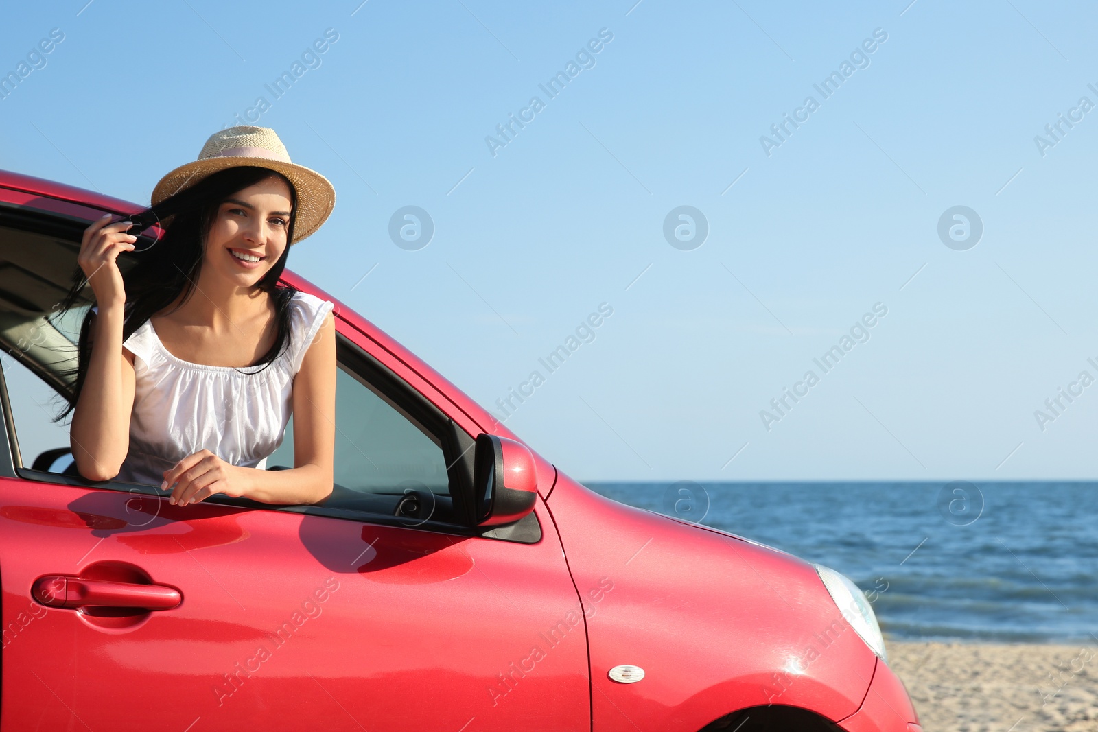 Photo of Happy young woman leaning out of car window on beach, space for text. Summer trip