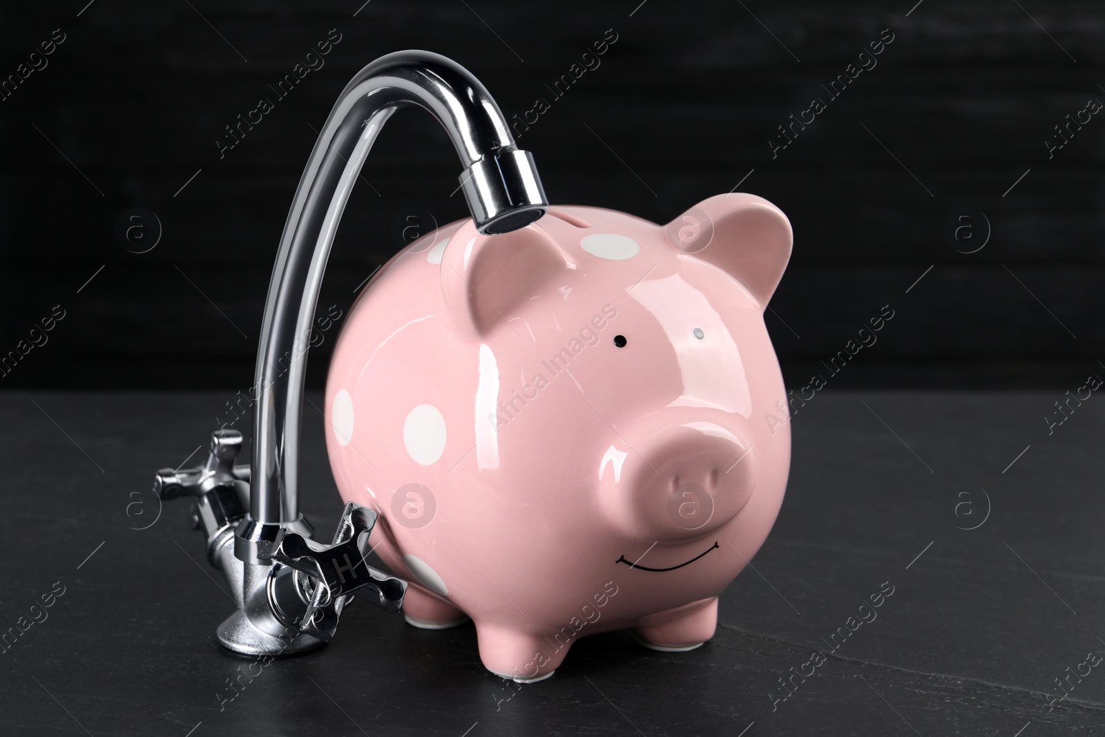 Photo of Water scarcity concept. Piggy bank and tap on dark table