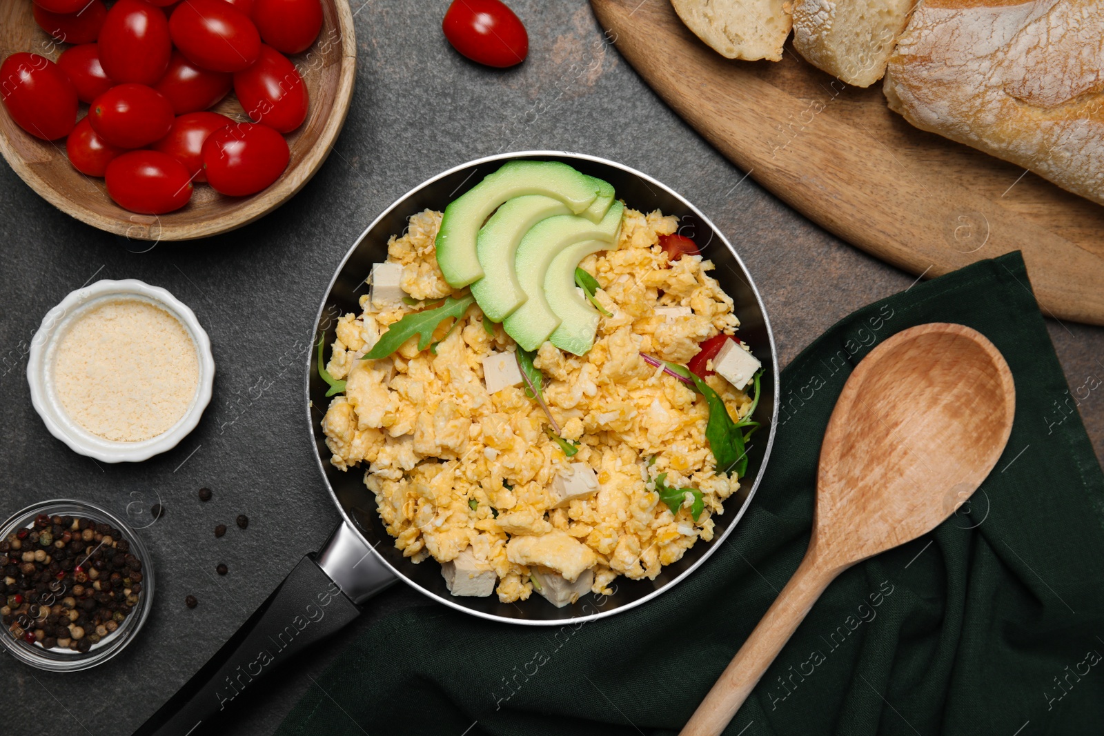 Photo of Frying pan with delicious scrambled eggs, tofu and avocado on black table, flat lay