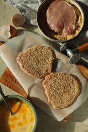 Photo of Cooking schnitzel. Raw pork chops in bread crumbs, meat mallet and ingredients on grey table, flat lay