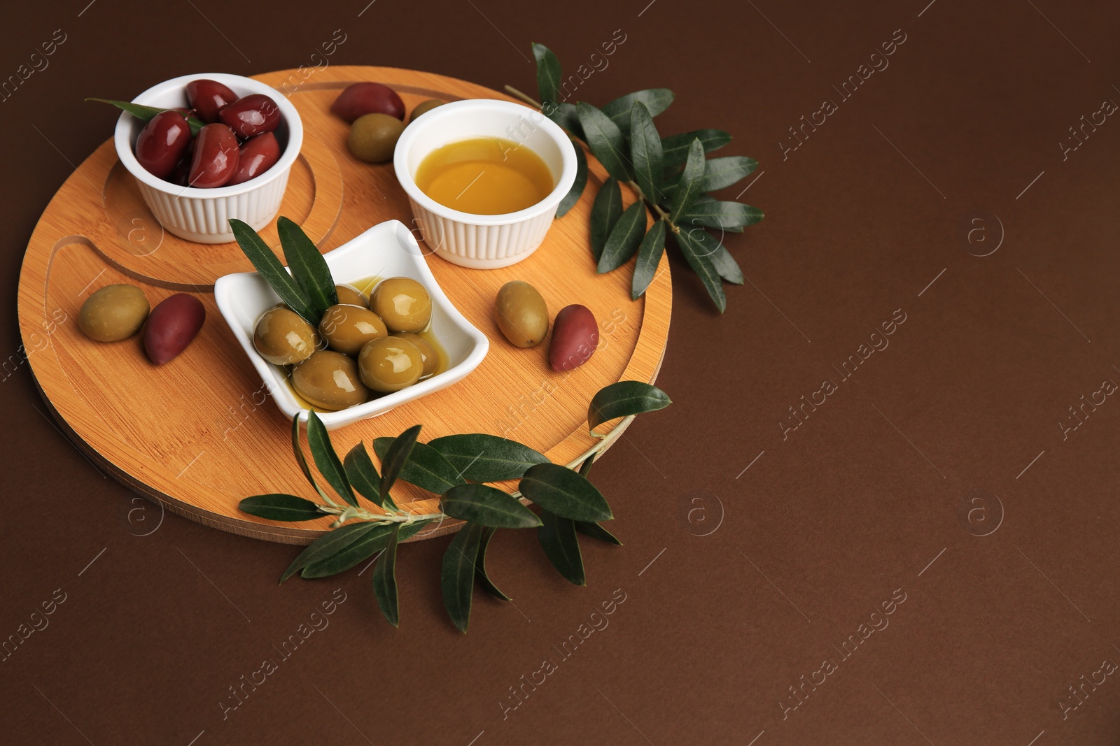 Photo of Bowl of oil, olives and tree twigs on brown table, space for text