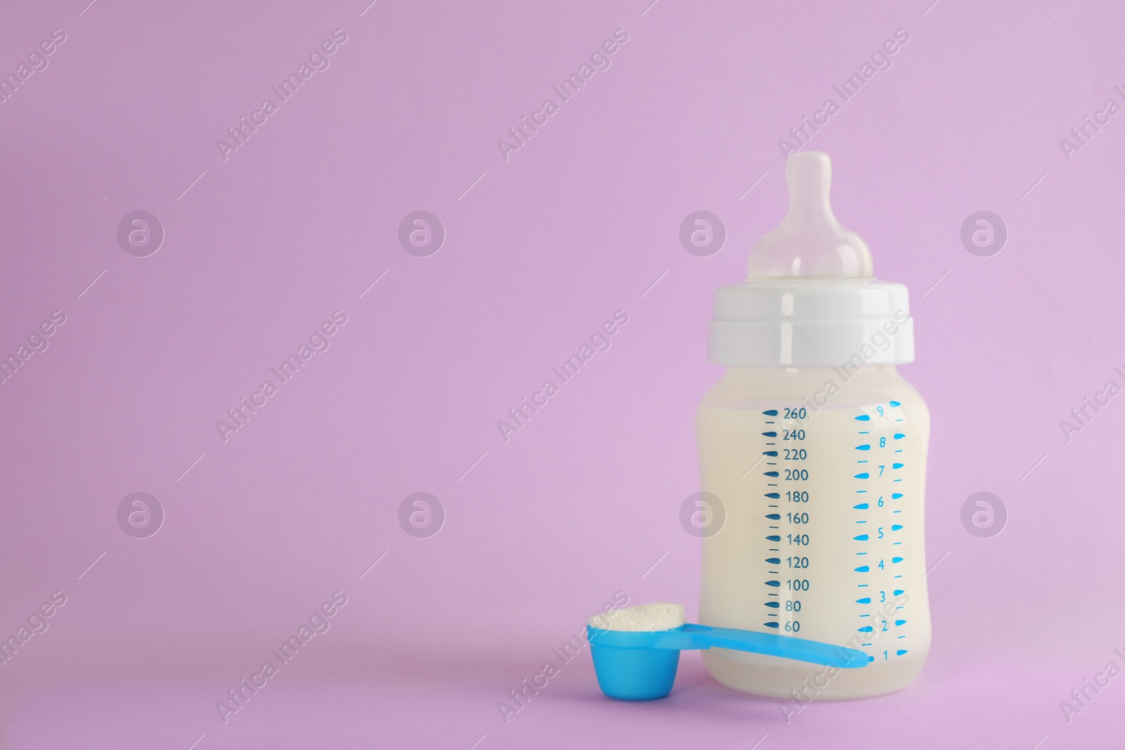 Photo of Feeding bottle with infant formula and scoop of powder on lilac background, space for text. Baby milk