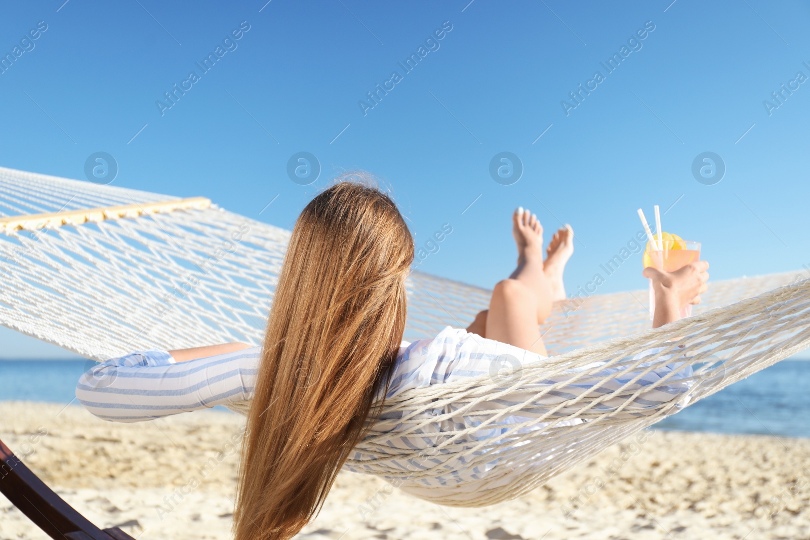 Photo of Young woman with refreshing cocktail relaxing in hammock on beach