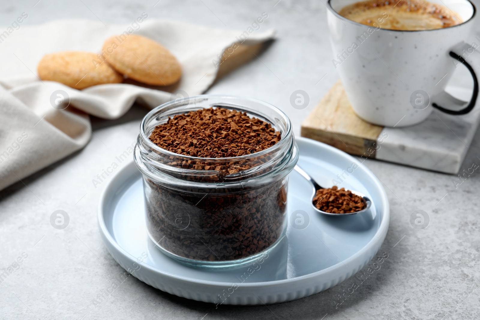 Photo of Spoon and glass jar with instant coffee on light table