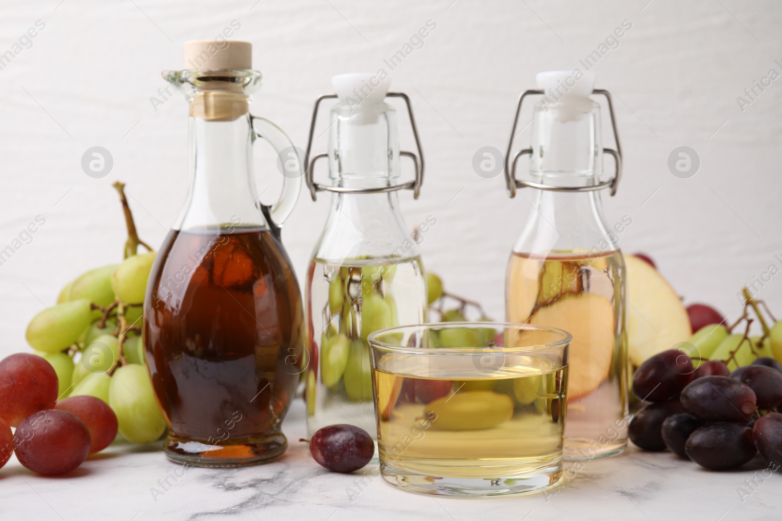 Photo of Different types of vinegar and grapes on light marble table, closeup