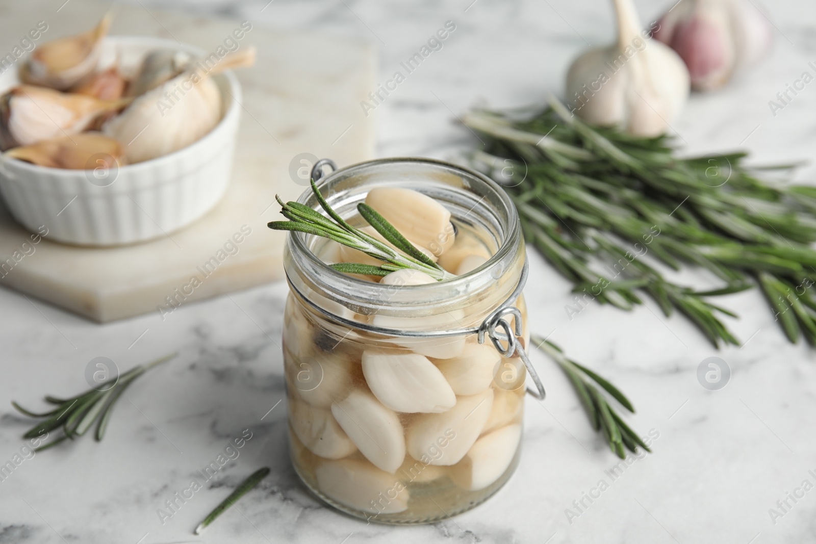 Photo of Composition with jar of pickled garlic on white marble table