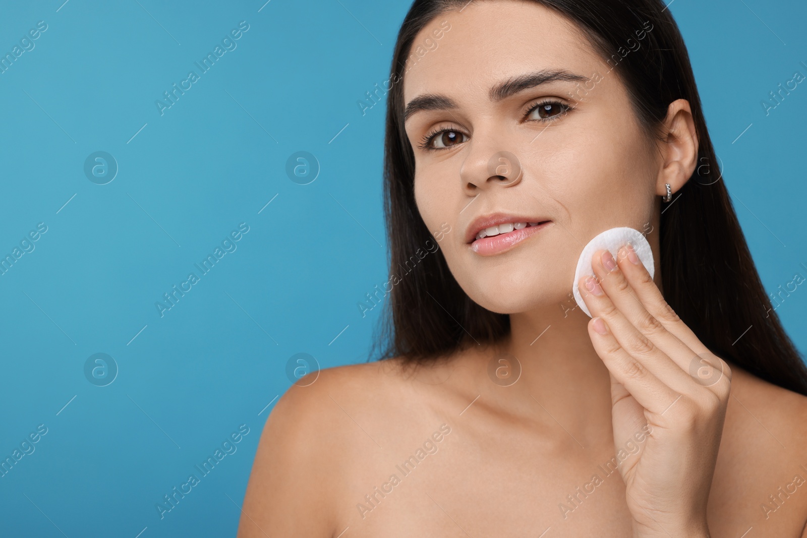 Photo of Young woman with cotton pad on light blue background. Space for text