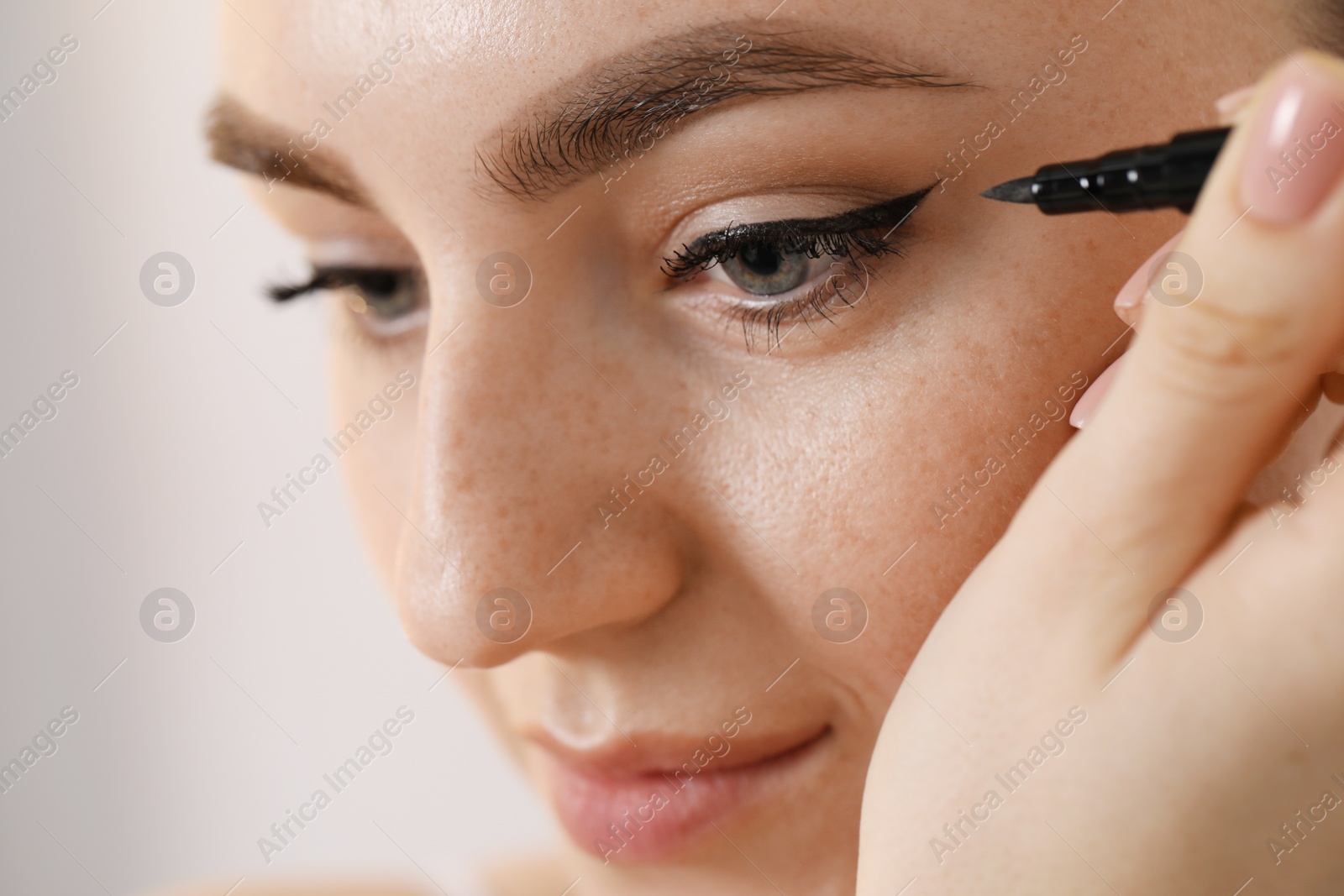 Photo of Makeup product. Woman applying black eyeliner on blurred background, closeup