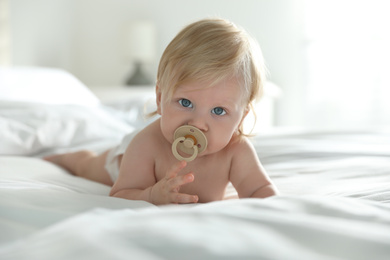 Photo of Cute little baby in diaper with pacifier lying on bed at home