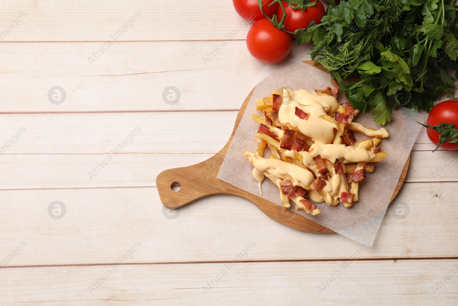 Photo of Delicious French fries with bacon, cheese sauce, tomatoes and herbs on wooden table, top view. Space for text