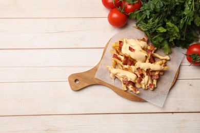 Photo of Delicious French fries with bacon, cheese sauce, tomatoes and herbs on wooden table, top view. Space for text