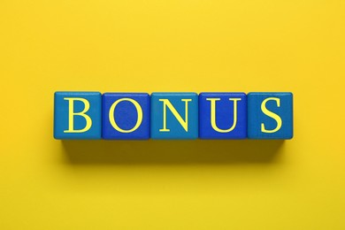 Word Bonus made of color cubes with letters on yellow background, top view