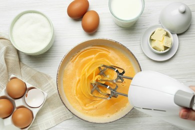 Woman beating eggs with mixer at white wooden table, top view
